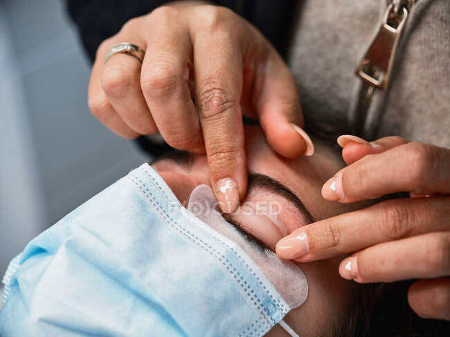 Crop anonymous beauty master applying lash lift shield on eyelid of female client during eyelash treatment in salon — Stock Photo