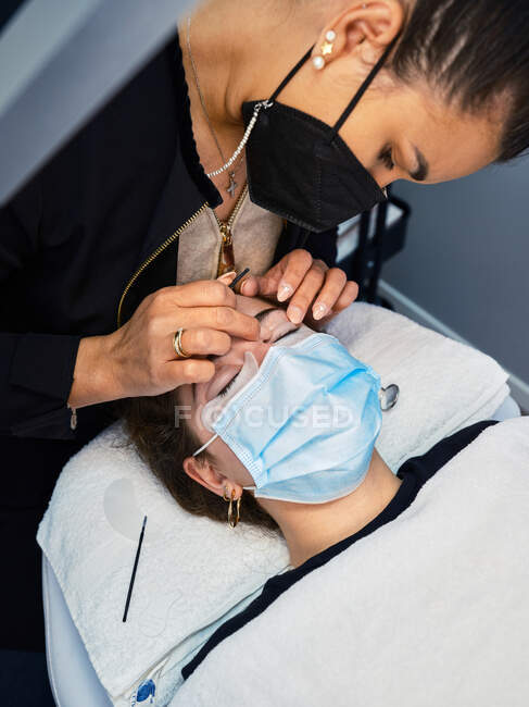 From above crop beauty master applying lash lift shield on eyelid of female client during eyelash treatment in salon — Stock Photo
