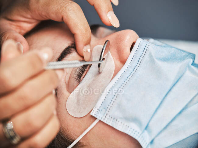 Crop cosmetician with professional mirror doing eyelash lamination for female client in modern beauty salon — Stock Photo