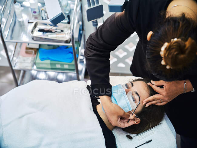 Von oben beschnittene anonyme Kosmetikerin mit Applikator, der die Augenbraue einer Kundin mit Vergangenheit für die Laminierung während der Schönheitsbehandlung im Salon bedeckt — Stockfoto