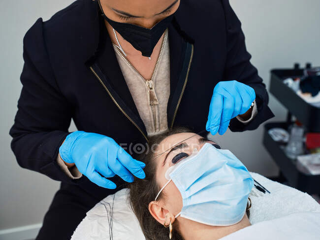 Professional cosmetician in latex gloves using thread to measure eyebrow of female client during beauty procedure in salon — Stock Photo