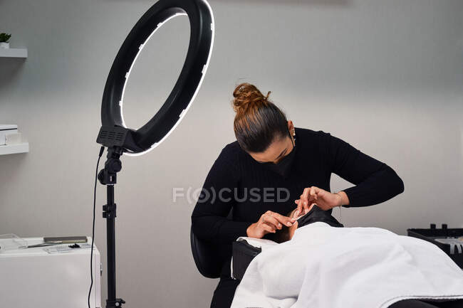 Beauty master applying lash lift shield on eyelid of female client during eyelash treatment in salon — Stock Photo