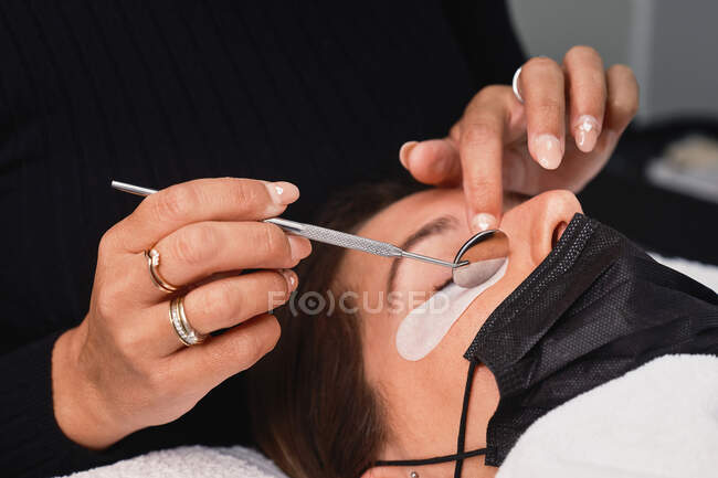 Cosmetician de colheita com espelho profissional fazendo laminação de pestanas para cliente feminino no salão de beleza moderno — Fotografia de Stock