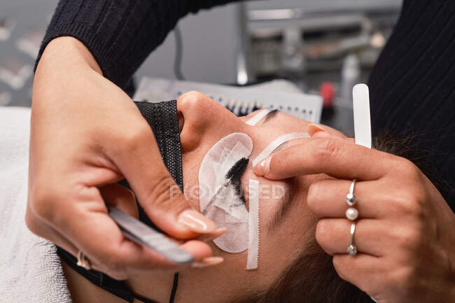 Seitenansicht der Ernte anonyme Kosmetikerin mit Pinsel auftragen Farbe auf Wimpern der Patientin während der Wimpernverlängerung Verfahren im Schönheitssalon — Stockfoto