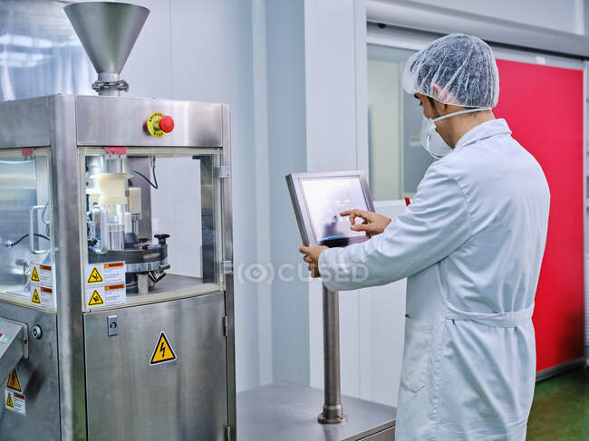 Vista laterale del chimico maschile in una riempitrice uniforme di capsule operative nello stabilimento di produzione farmaceutica — Foto stock