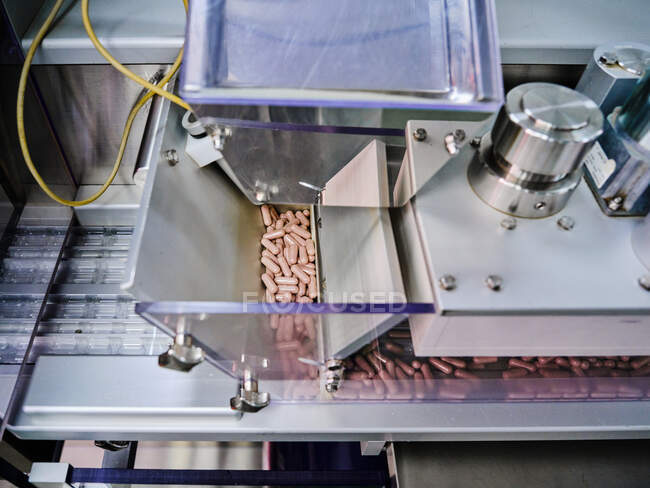 Сучасна фармацевтична машина з купою рожевих таблеток на конвеєрі, розміщеному у виробничій лабораторії — стокове фото