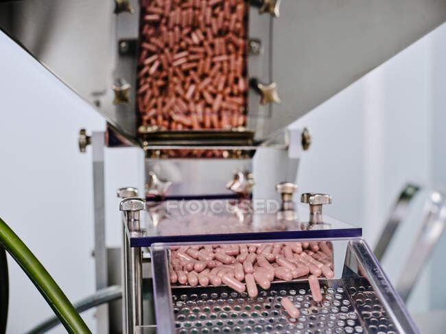 Máquina farmacéutica contemporánea con pilas de píldoras rosadas en el transportador colocado en el laboratorio de fabricación - foto de stock