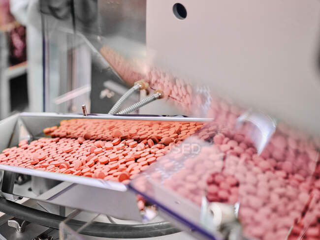 Macchina farmaceutica contemporanea con pile di pillole rosa su trasportatore poste in laboratorio di produzione — Foto stock