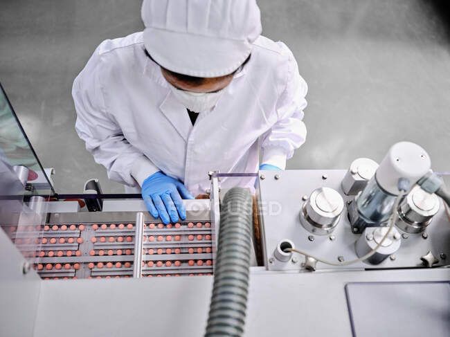 Von oben eine Fabrikarbeiterin in Uniform, die im Labor der pharmazeutischen Fertigung ein Förderband mit Pillen bedient — Stockfoto