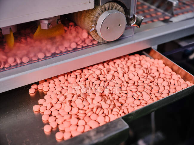 Contemporary pharmaceutical machine with piles of pink pills on conveyor placed in manufacturing laboratory — Stock Photo