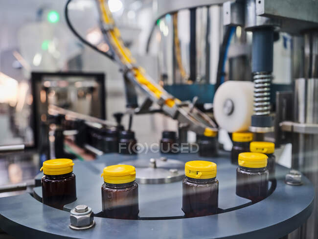 Frascos de plástico con medicamentos en el transportador de la máquina de tapado en el laboratorio de fabricación farmacéutica - foto de stock