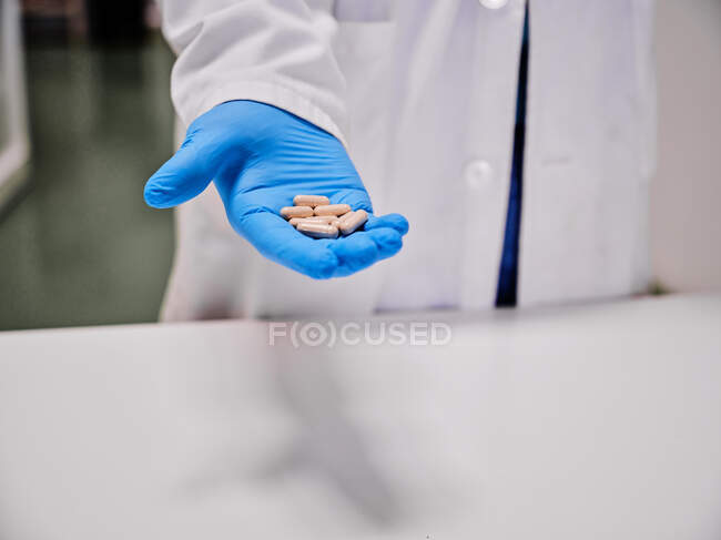Crop cientista anônimo em luvas de proteção em pé com pilha de cápsulas em laboratório — Fotografia de Stock