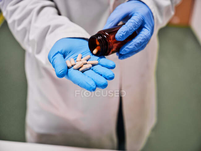 Crop cientista anônimo em luvas de proteção em pé com pilha de cápsulas em laboratório — Fotografia de Stock