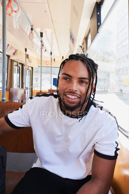 Jeune homme afro-américain positif en vêtements décontractés assis dans le train sur le chemin de fer Viena dans la journée en ville — Photo de stock