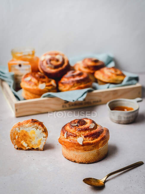 Many fresh cinnamon buns with almond flakes served with jam and honey on tray covered with fabric in morning — Stock Photo