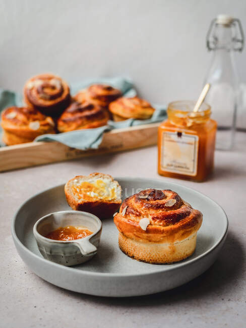 Viele frische Zimtbrötchen mit Mandelflocken, serviert mit Marmelade und Honig auf einem mit Stoff bedeckten Tablett am Morgen — Stockfoto