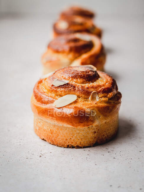 Soft focus of delicious cinnamon buns with almond flakes arranged in line on gray table — Stock Photo