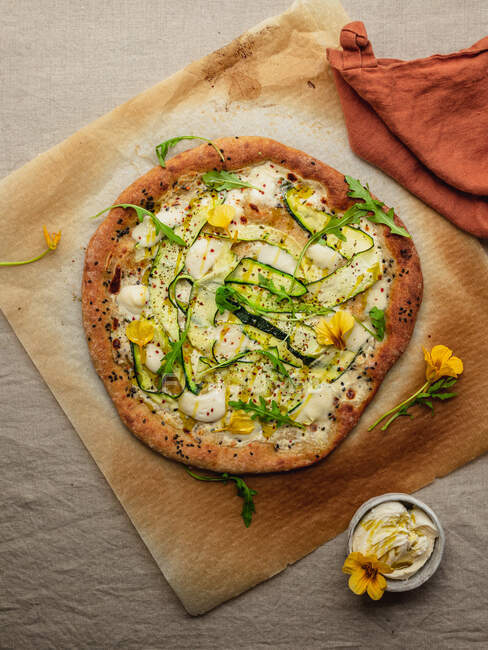 Vista superior de la sabrosa pizza con rodajas de calabaza y condimentos con hojas de rúcula frescas sobre papel pergamino sobre fondo beige - foto de stock