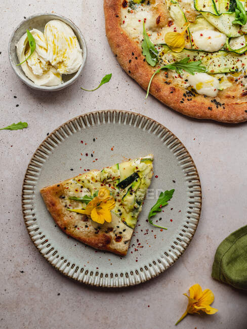Overhead view of appetizing slice of pizza with arugula leaves and squash flower on melted cheese on gray background — Stock Photo