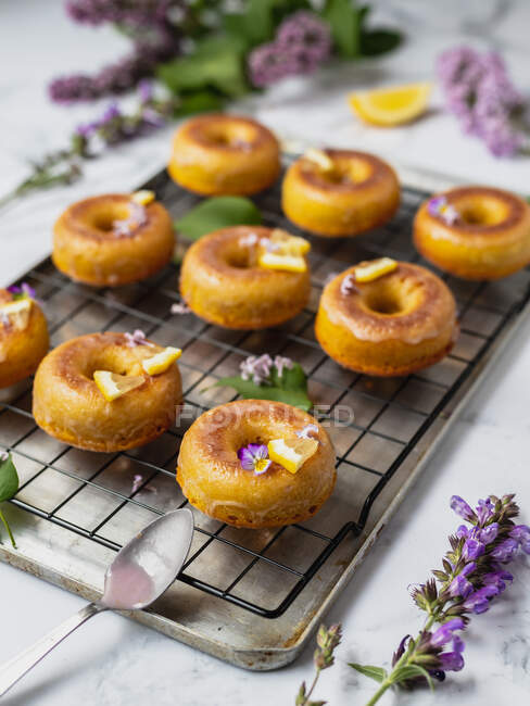 Von oben schmackhafte Donuts auf Kühlregal mit Blättern zwischen blühenden Lavendelzweigen auf Marmoroberfläche — Stockfoto