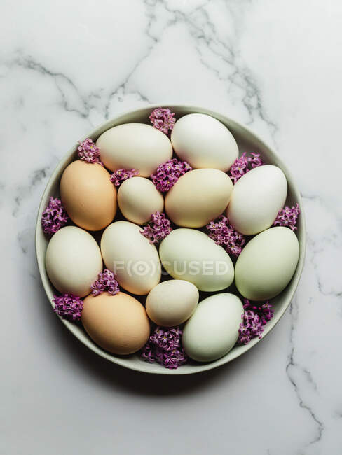 Overhead view of raw chicken eggs on round shaped plate with blossoming Lavandula flowers on marble surface — Stock Photo