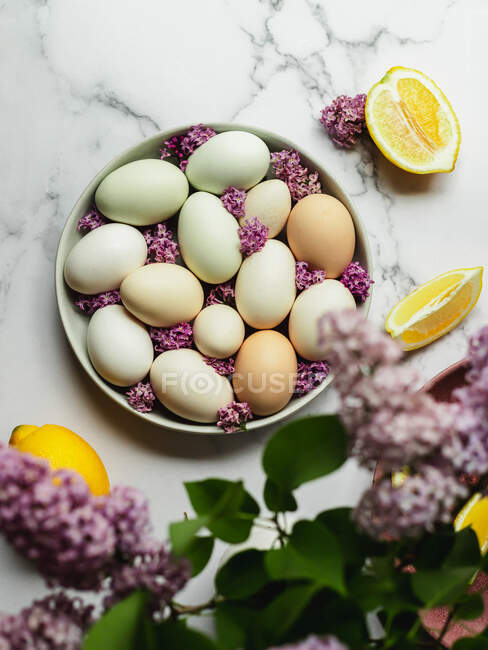 Верхний вид куриных яиц на тарелке среди цветущих цветов Лаванды и свежих ломтиков лимона — стоковое фото