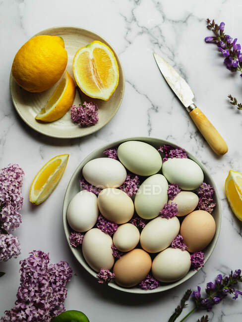 Vue du dessus des œufs de poulet dans une assiette parmi les fleurs de Lavandula en fleurs et les tranches de citron frais avec couteau — Photo de stock
