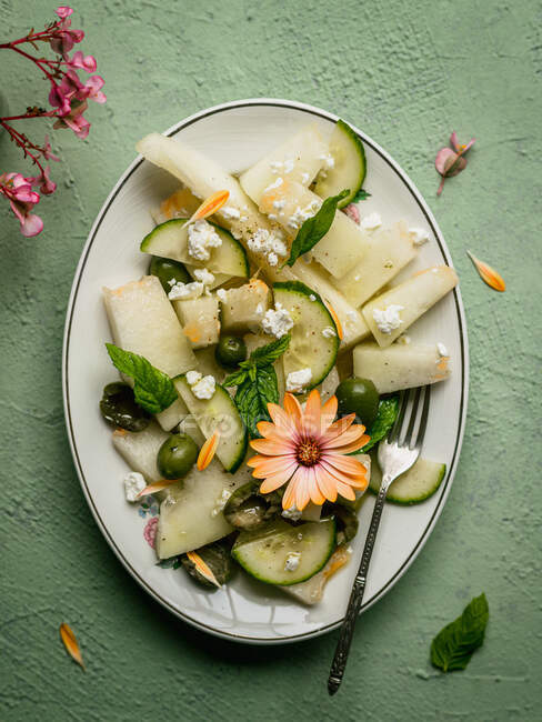 Vue du dessus de délicieuse salade de melon avec des concombres et des olives servis dans une assiette avec des herbes près salière et serviette sur fond vert — Photo de stock