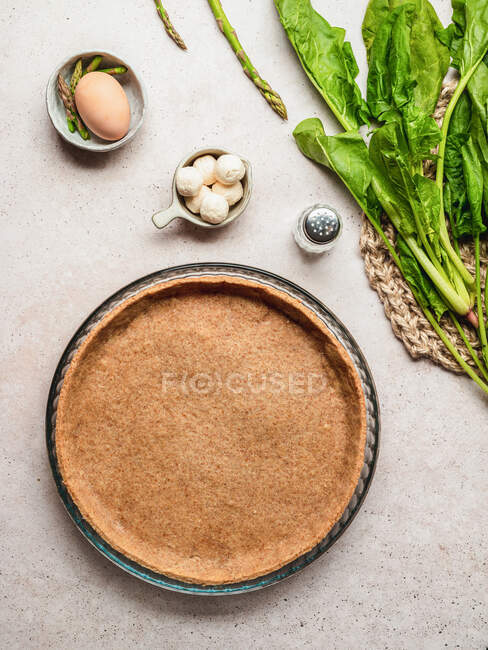Top view of spinach and asparagus with egg and mozzarella cheese placed near pastry base for quiche preparation — Stock Photo