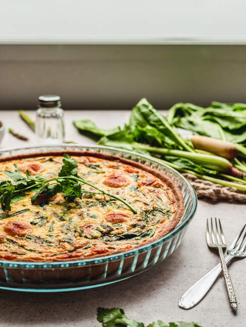 Deliziosa quiche con prezzemolo posto vicino all'uovo e spinaci freschi con asparagi sul tavolo — Foto stock
