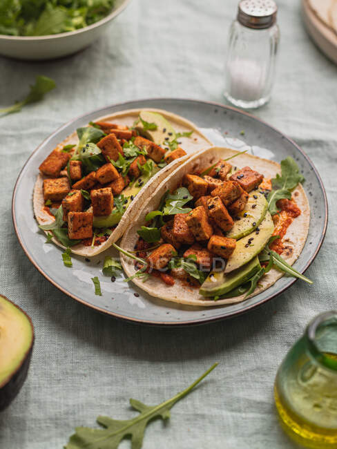 Von oben Tortillas mit gebratenen Tofuwürfeln und Avocadostücken mit frischen Rucolablättern auf Tischdecke — Stockfoto