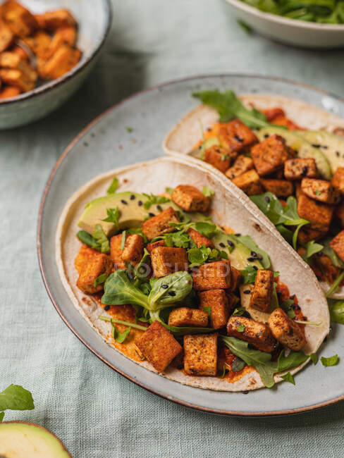 From above tortillas with fried tofu cubes and avocado pieces with fresh arugula leaves on tablecloth — Stock Photo
