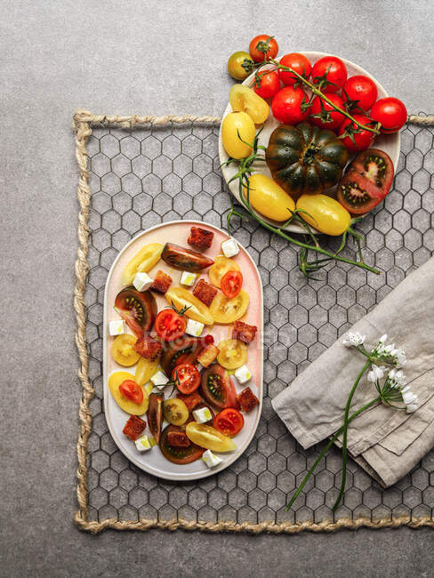 Vista dall'alto dell'insalata vegetariana di pomodoro con cubetti di formaggio feta serviti su piatto su tavolo di cemento grigio — Foto stock