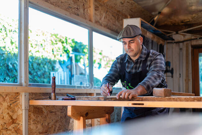 Lenhador adulto experiente com lápis e régua marcando placa de madeira enquanto trabalhava na bancada na oficina de carpintaria — Fotografia de Stock