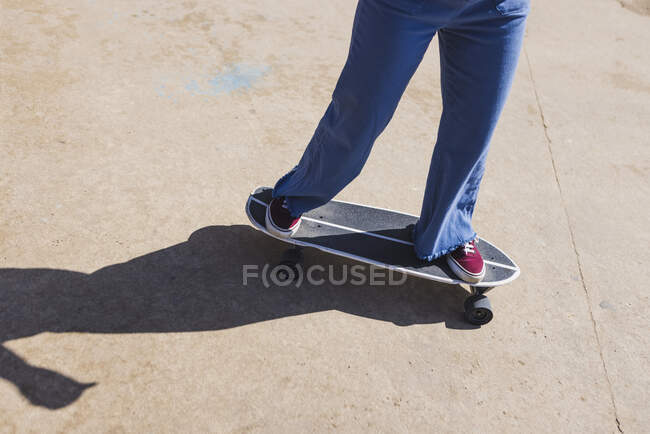 Зверху невизначеної спортивної жінки в кросівках, що стоять на скейтборді на тротуарі під час тренувань у місті — стокове фото
