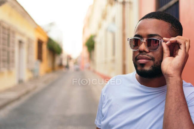 Afro-Américain avec des lunettes de soleil marchant dans la rue de la ville en regardant la caméra. — Photo de stock
