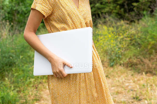 Crop anonymous female freelancer holding laptop while standing in summer park — Stock Photo