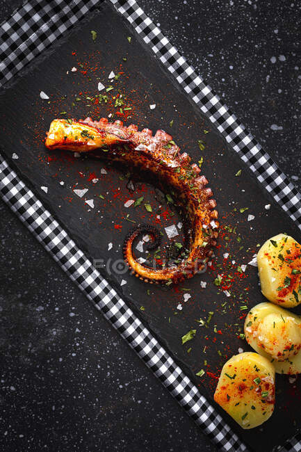 Vista superior do tentáculo de polvo frito e pedaços de batata servidos com especiarias na placa preta na mesa — Fotografia de Stock