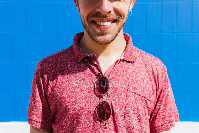 Нерозпізнаний молодий бородатий самець у стильному повсякденному вбранні і кепка насолоджуючись літнім днем біля блакитної стіни на міській вулиці. — стокове фото