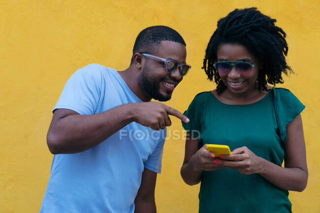 Casal preto usando um telefone celular encostado a uma parede amarela — Fotografia de Stock