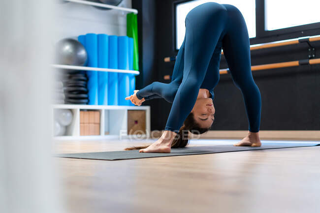 Visão traseira de corpo inteiro de focado flexível jovem do sexo feminino fazendo de pé para a frente curvar com postura abridor de ombro enquanto pratica ioga no estúdio de fitness — Fotografia de Stock