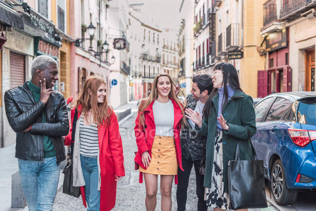 Company of happy multiracial friends in stylish clothes walking together in city street during weekend — Stock Photo