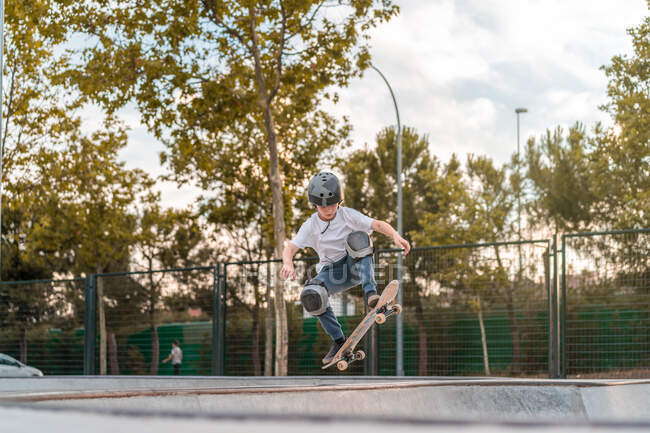 Adolescente saltando con monopatín y mostrando truco en rampa en skate park - foto de stock