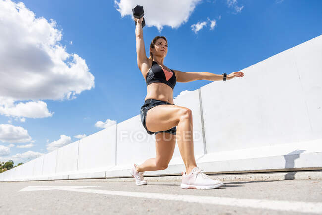 Junge Frau trainiert mit Hantel im Freien, Arm nach unten und gebeugtes Knie, Seitenansicht — Stockfoto