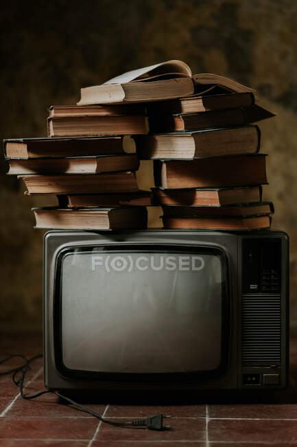 Купа книжок, розміщених на старовинному телевізорі на потертій покришками підлозі. — стокове фото