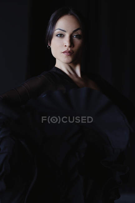 Young self assured female with deep gaze in black apparel and earring looking at camera — Stock Photo