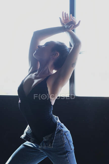 Young barefoot female in jeans with hair bun dancing while looking up on floor with shadows in sunlight — Stock Photo