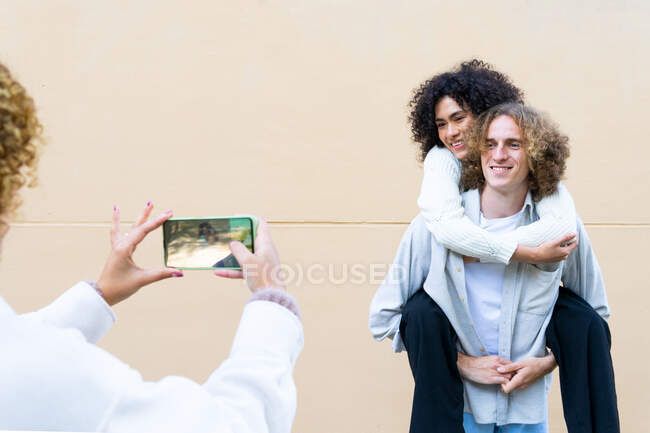 Mulher de colheita tirando foto de homem rindo dando passeio de piggyback para mulher étnica todos com cabelo encaracolado — Fotografia de Stock
