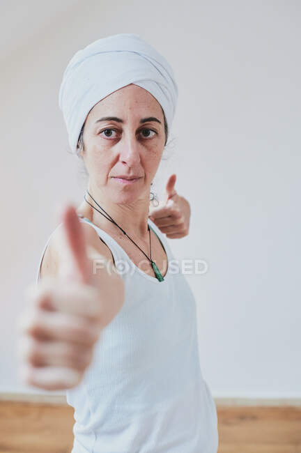 Femme d'âge moyen dans le bandeau pratiquant le yoga tout en montrant comme geste et regardant vers l'avant sur fond blanc — Photo de stock