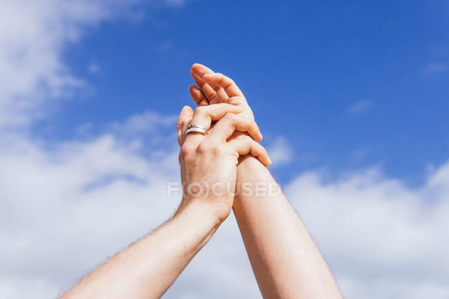 Low angle of hands of crop unrecognizable person with ring on finger against blue cloudy sky in sunny summer day — Stock Photo